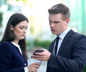 Man and woman dressed in business suits look at a mobile phone with concerned expressions.